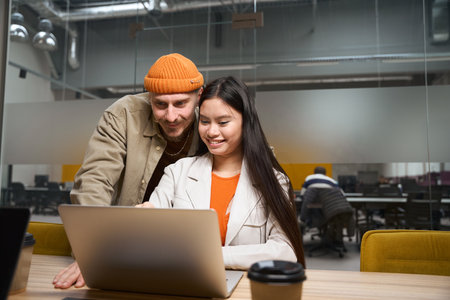 Joyous company employee showing something on laptop screen to colleagueの写真素材