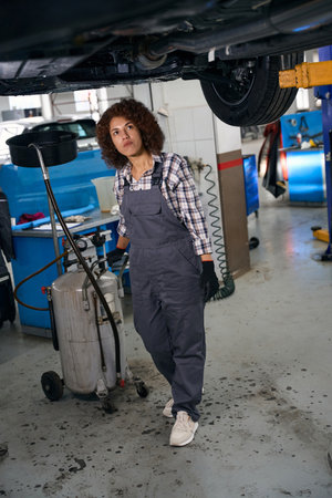 Multiracial female automechanic standing under car with brake fluid drain tankの写真素材