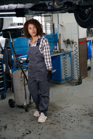 Multiracial workshop worker standing under car with brake fluid drain tankの写真素材