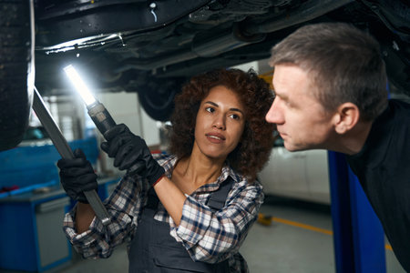 Multiracial female mechanic and customer inspecting the car from belowの写真素材