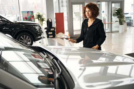 Smiling multiracial woman stands near a new carの写真素材