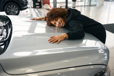 Happy multiracial woman hugging the hood of a new carの写真素材