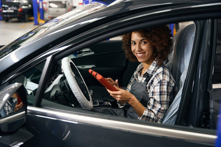 Smiling multiracial master sits in car with apparatus for computer diagnostics