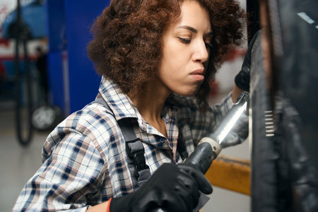 Multiracial woman in a plaid shirt carefully examines wheel carの写真素材