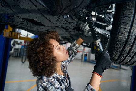 Pretty female repairman with special tool inspects car from belowの写真素材