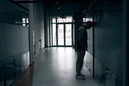 Depressed company employee standing alone in dark office corridorの写真素材