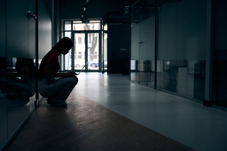 Focused corporate worker using laptop in dark empty office corridorの写真素材