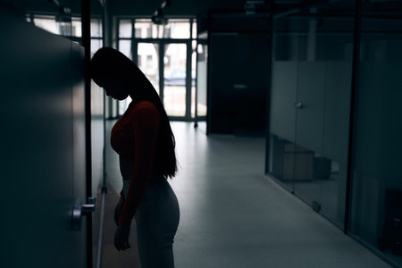 Despondent female office worker standing alone in dark empty corridorの写真素材