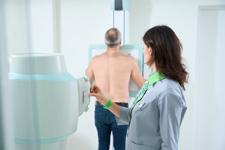 Female doctor adjusting equipment while male patient scanning chestの写真素材