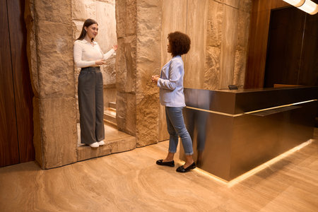 Responsible female receptionist informing pretty client at corridorの写真素材