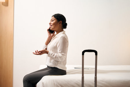 Joyful female entrepreneur talking on smartphone in her hotel roomの写真素材