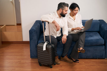 Interracial tourist couple using laptop in hotel roomの写真素材
