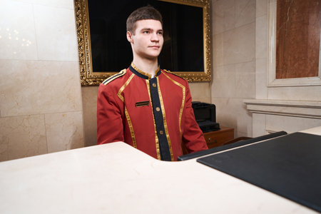 Young pleasant bellhop is standing at the reception deskの写真素材