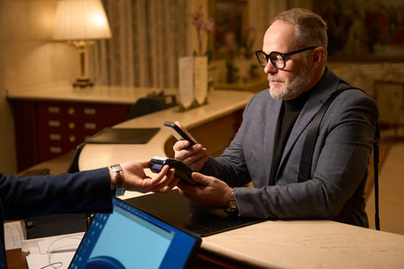 Gray-haired traveler in a hotel makes a payment through the terminalの写真素材