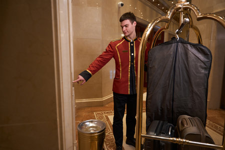 Young bellboy is pushing a cart with luggage around lobbyの写真素材