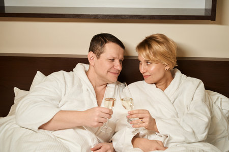 Middle-aged couple in love enjoying champagne in bedの写真素材