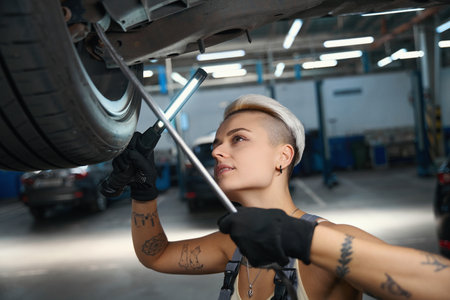 Woman works with a car raised on a liftの写真素材