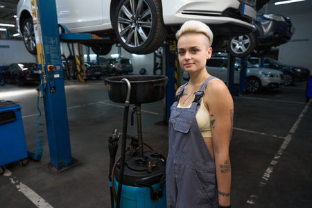 Woman auto repairman stands with a device for draining oilの写真素材