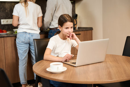 Cute girl sitting at table with laptop in kitchen in hotel roomの写真素材