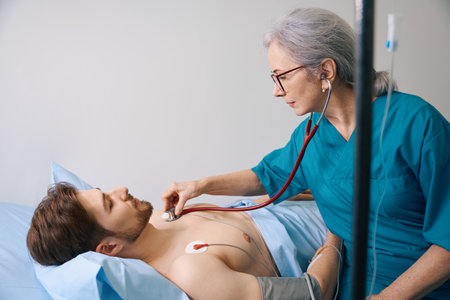 Experienced elderly doctor listens with a stethoscope to young patientの写真素材