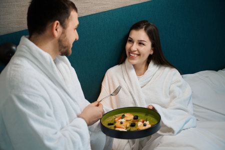 Young man treats his wife to breakfast in the bedroomの写真素材