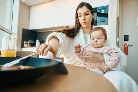 Long-haired mother sits with a small child in the kitchenの写真素材