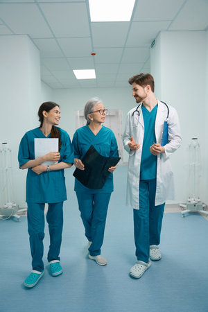 Man and two women in medical uniforms walk along hospital corridorの写真素材
