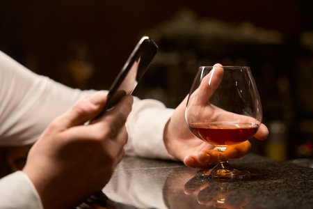 Male hands holding smartphone and glass of whiskey at bar counterの写真素材