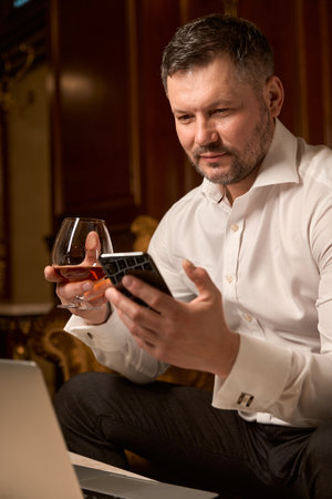 Handsome man with smartphone alone and glass of whiskey in restaurantの写真素材