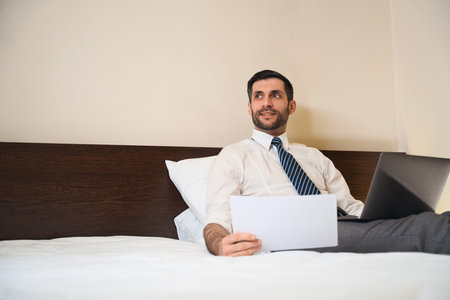 Man half-sitting on pillows, settled down on a bedの写真素材