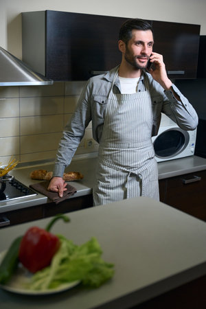 Brunette in chefs apron stands in the kitchen with phone