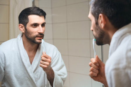 Male with a toothbrush stands in front of a mirrorの写真素材