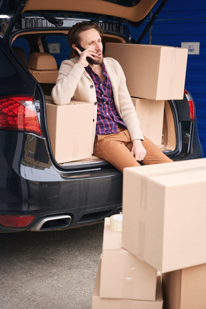 Young guy with cardboard boxes in car trunk at storage warehouseの写真素材