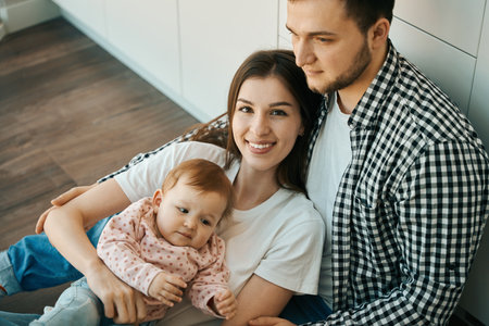 Joyful mom and dad are hugging the baby on the floor in the kitchen