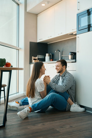 Laughing young spouses sit embracing on floor in the kitchenの写真素材