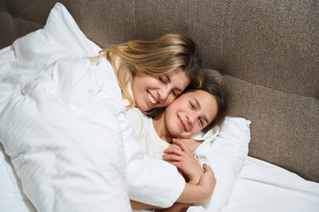 Smiling woman and daughter relaxing in the bedroomの写真素材