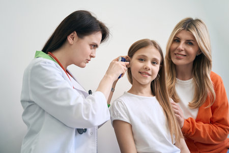 Concentrated woman laryngologist examining ear of little patient with otoscopeの写真素材