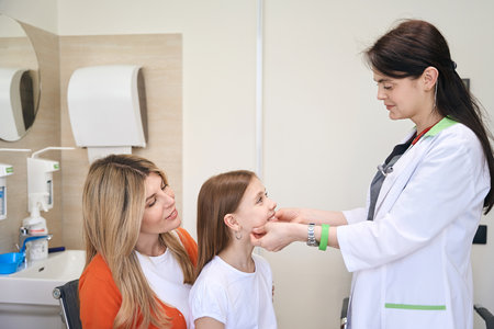 Little girl sitting on mother knees while pediatrician checking her lymph nodesの写真素材