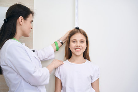 Woman nurse checking little girl height using special measuring plankの写真素材