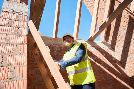 Male foreman in hardhat and safety vest standing on wooden ladder
