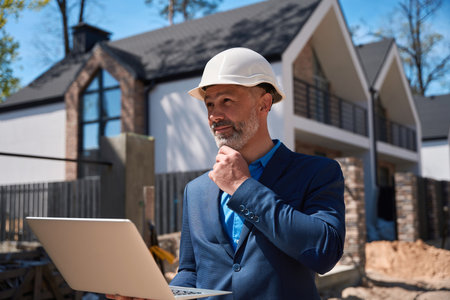 Architect walking at construction site in hardhat, using laptopの写真素材