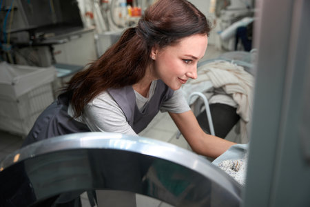 Woman laundry service operator taking clothes out of the washing machineの写真素材
