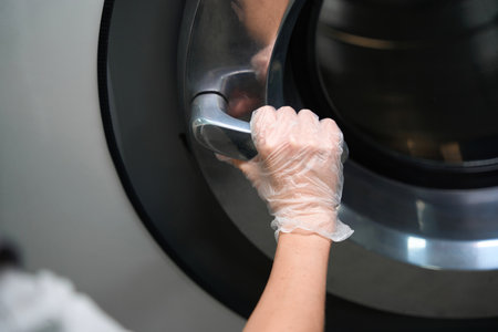 Woman in protective gloves holding big industrial washing machine handleの写真素材