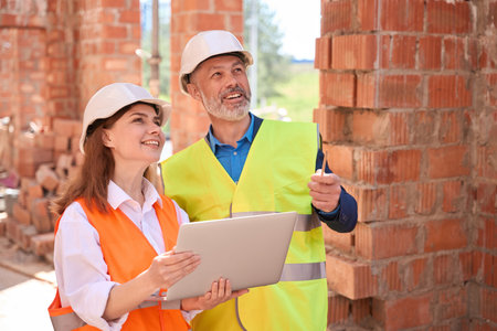 Smiling building engineers in hardhats planning design holding laptop with app