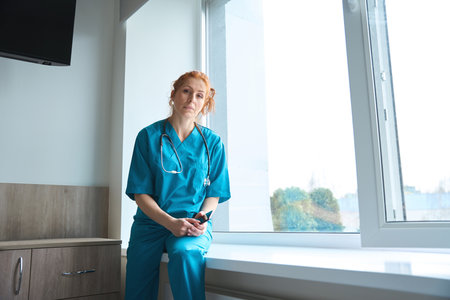 Female doctor sitting on the windowsill in hospitalの写真素材