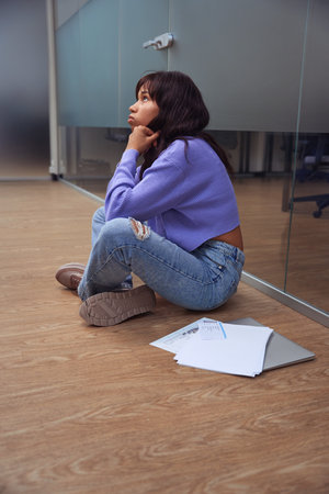 Thoughtful female freelancer sitting on floor indoors