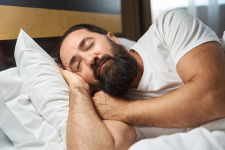 Bearded man sleeps in a bright hotel roomの写真素材