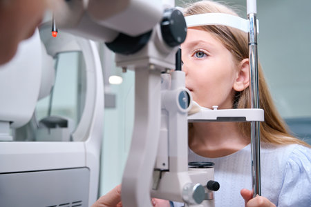 Focused little girl undergoing eye exam on ophthalmic device