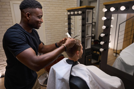 African American hairdresser gives a haircut to a young manの写真素材