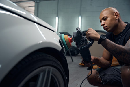 African American auto-mechanic carefully polishing car headlightsの写真素材